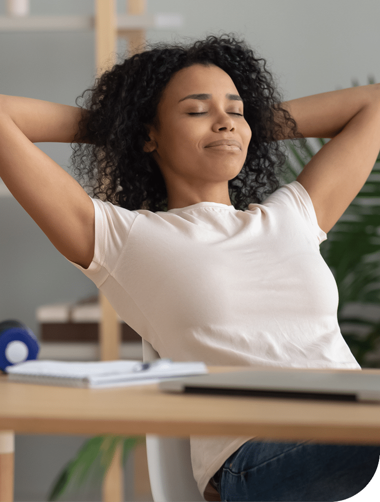 A woman rests back in her office chair with her eyes shut looking calm, wearing a white t-shirt