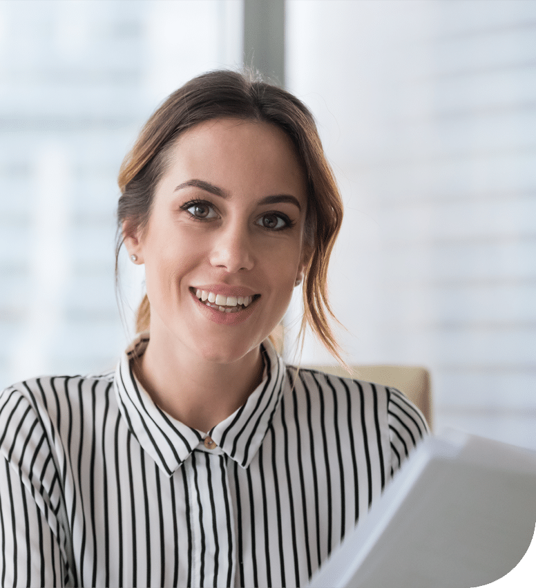 A woman is smiling towards the camera wearing a shirt against a white office background