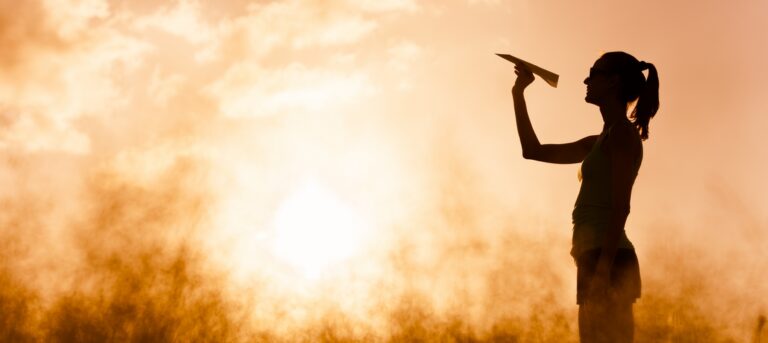 Woman launching a paper plane against a golden sunset